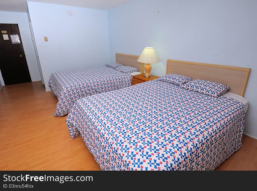 Large and simple room in hotel with double beds and wooden flooring.