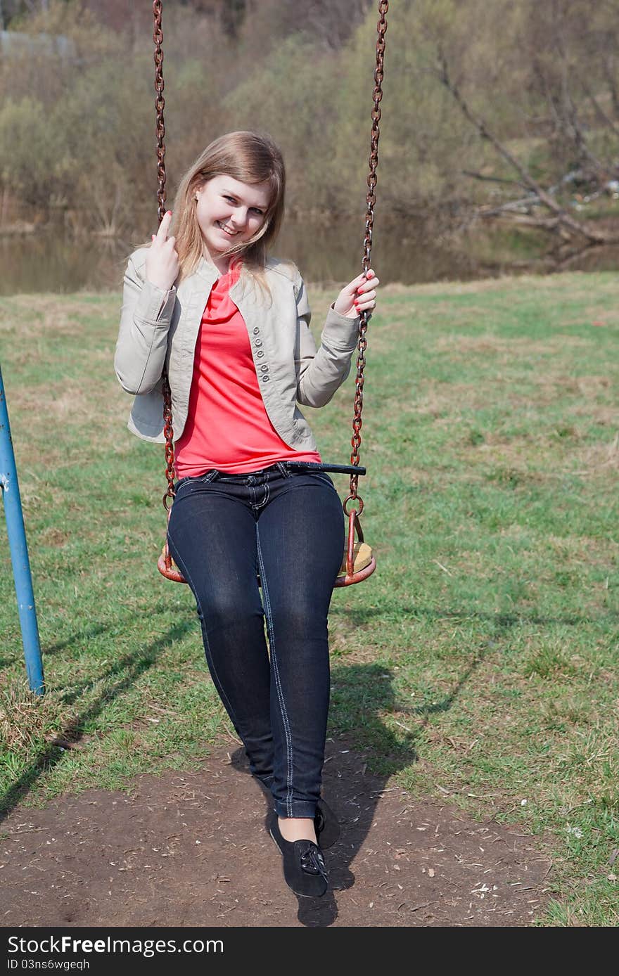 Young girl in the spring park sitting on the swing and smiling. Young girl in the spring park sitting on the swing and smiling