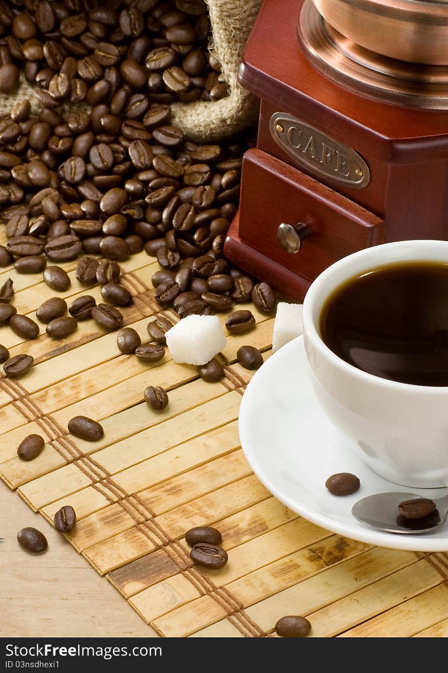 Cup of coffee and grinder with roasted beans on wooden background