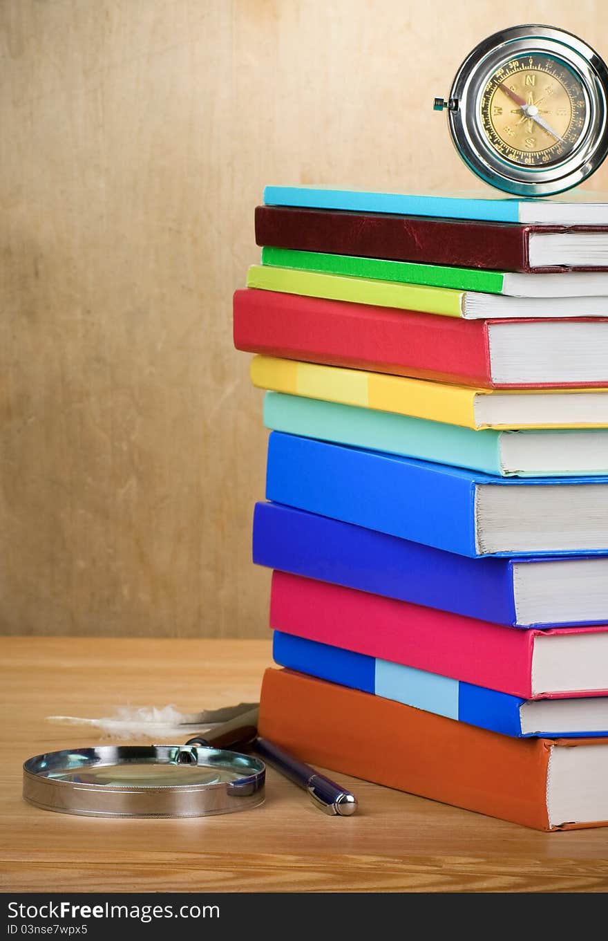 Pile of books, magnifier and compass with feather on wooden background