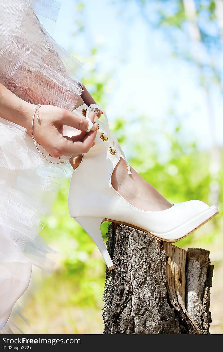 Bride lacing white shoes in the forest