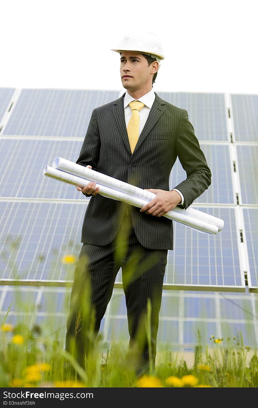 Male engineer at solar power station holding blueprints.