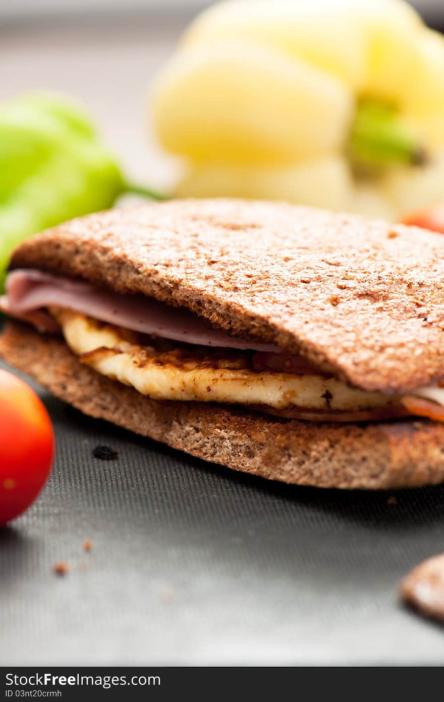 Cheese, ham and tomato sandwich with whole rye bread on a cutting board. Cheese, ham and tomato sandwich with whole rye bread on a cutting board.