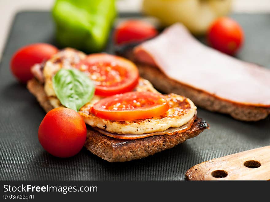 A cheese, ham, tomato and basil sandwich with whole rye bread on a cutting board with wooden utensil. A cheese, ham, tomato and basil sandwich with whole rye bread on a cutting board with wooden utensil.