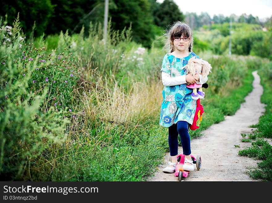 Cute child girl poses outdoors with baby doll