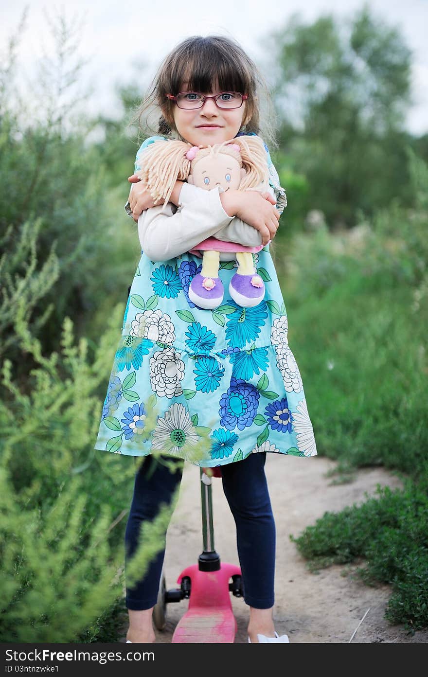 Cute Child Girl Poses With Baby Doll And Scooter