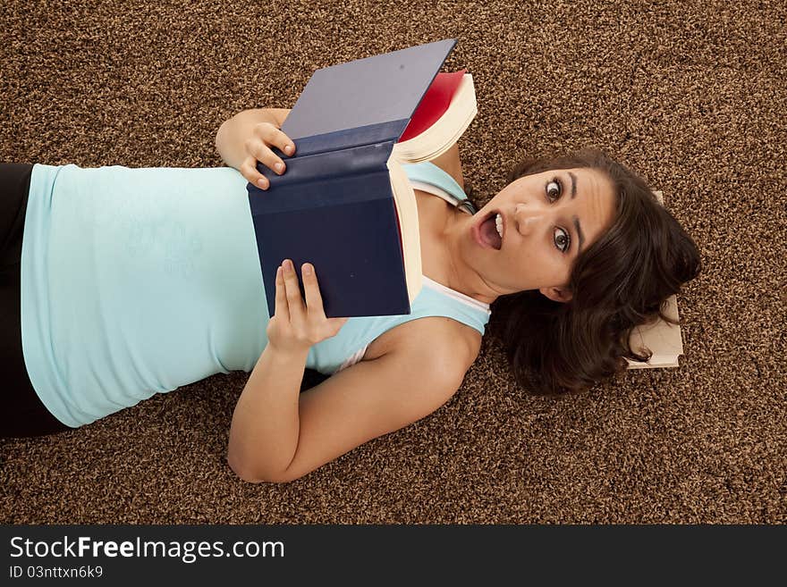 A woman with a shocked expression on her face while laying down reading a book. A woman with a shocked expression on her face while laying down reading a book.