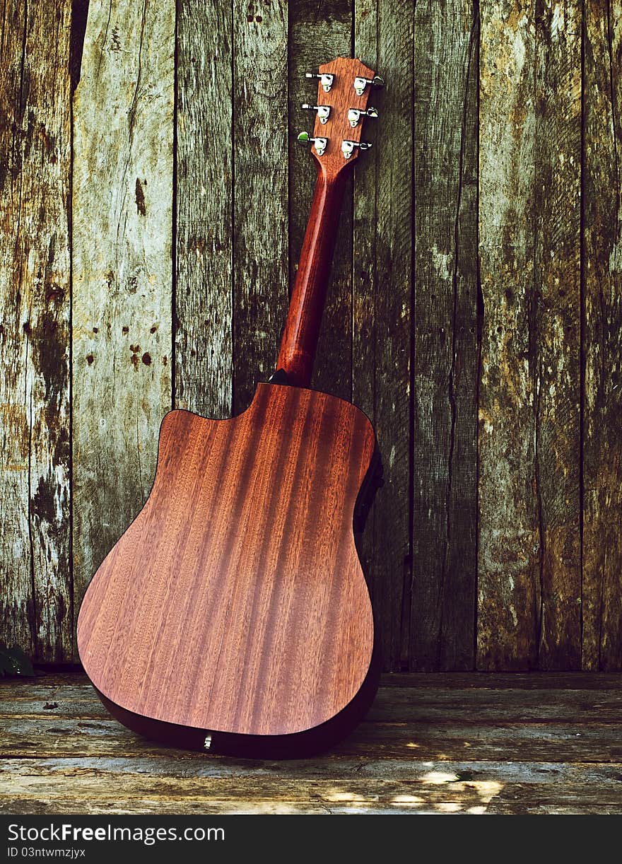 Richly toned back view of a classical guitar on a grunge wood backdrop with copy space. Richly toned back view of a classical guitar on a grunge wood backdrop with copy space.