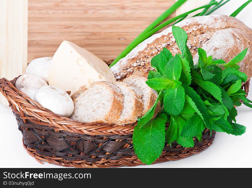 The wooden basket with mushrooms, bread, cheese, mint, and green onions. The wooden basket with mushrooms, bread, cheese, mint, and green onions