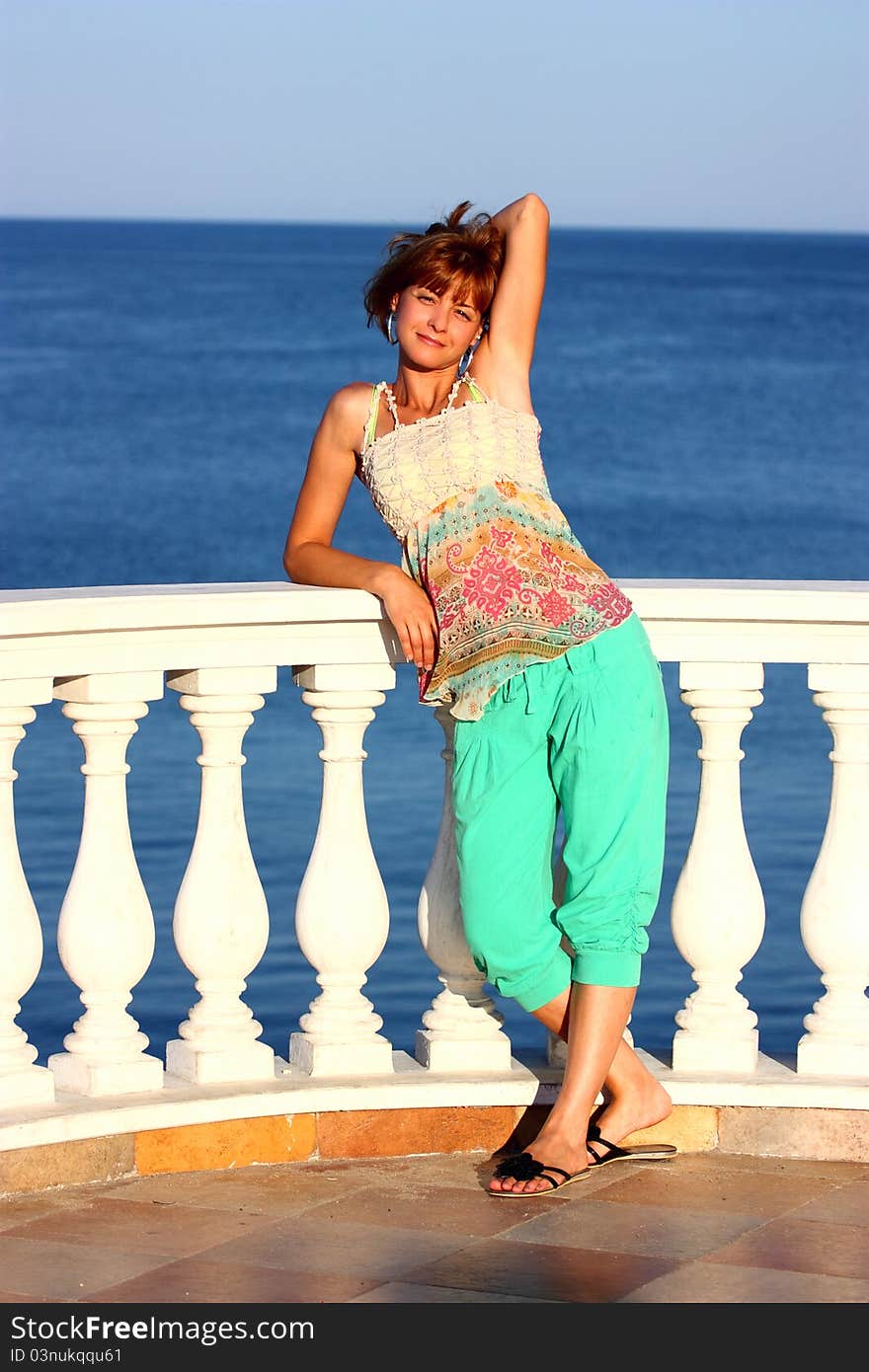 A beautiful woman on a balcony by the sea holding his hair. A beautiful woman on a balcony by the sea holding his hair