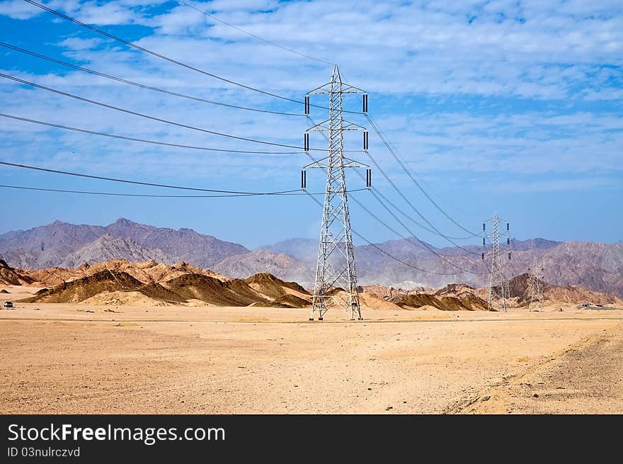 High voltage power electricity pylon line in the sand and the mountains