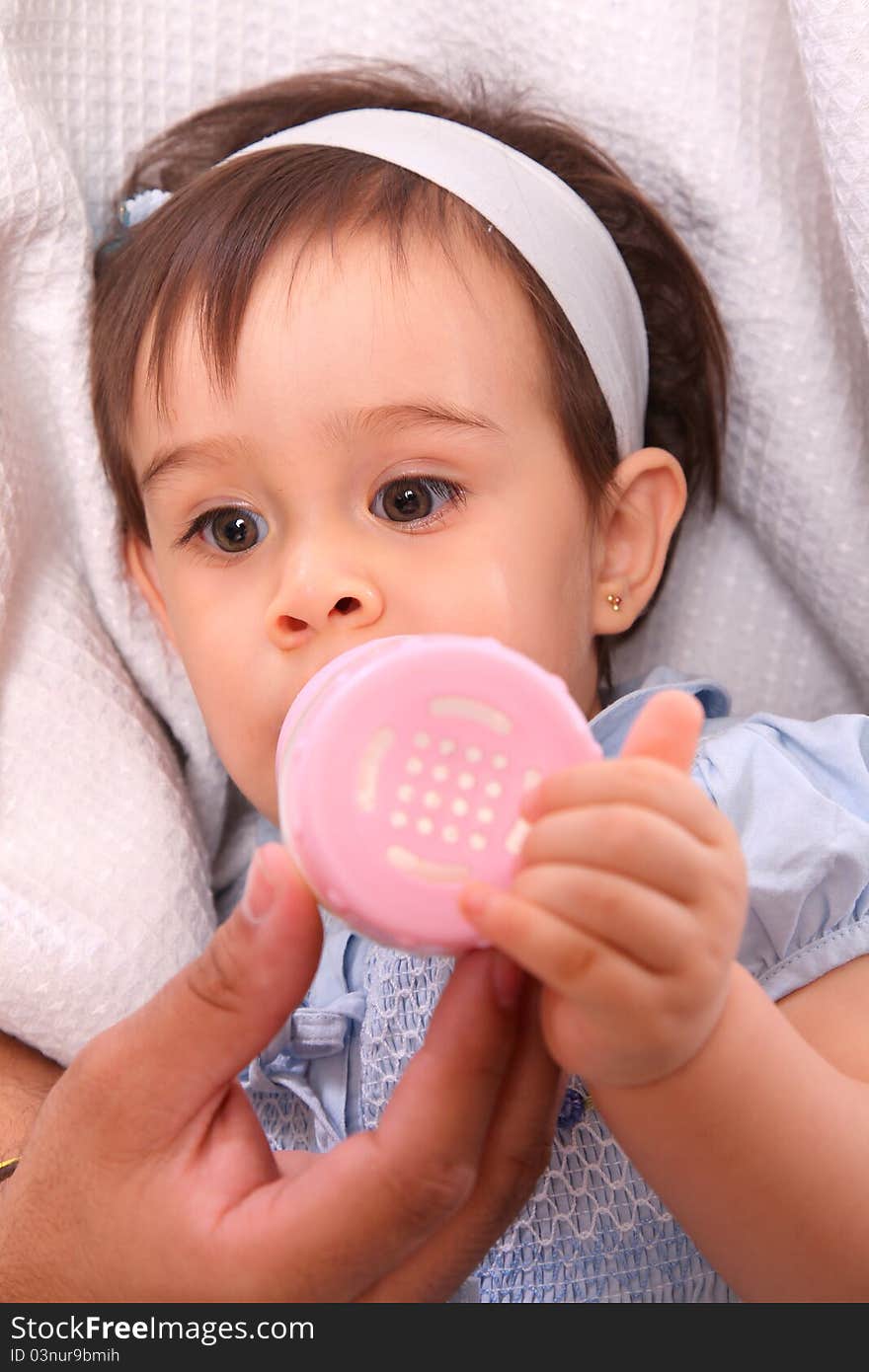 Baby girl with hair band and blue dress with pink bottle over bed. Baby girl with hair band and blue dress with pink bottle over bed