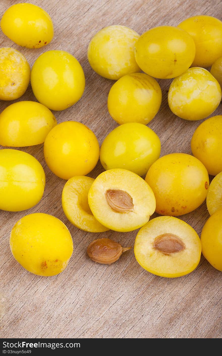 Studio-shot of small yellow plums also known as mellow mirabelles, on a wooden board.