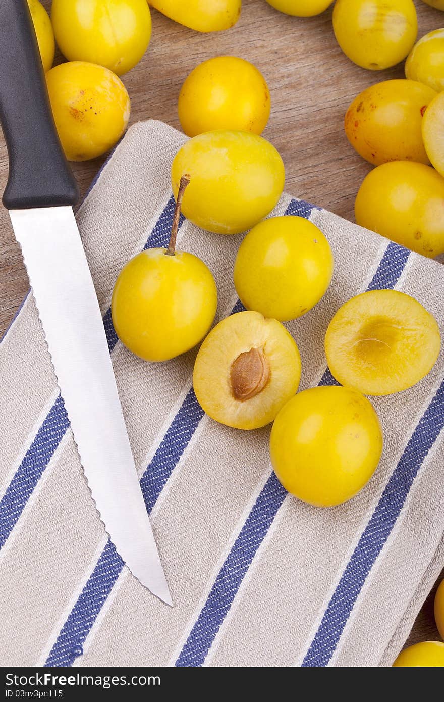 Studio-shot of small yellow plums also known as mellow mirabelles, on a dishtowel. one is halved with a knife.