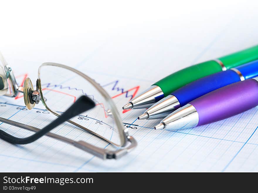 Extreme closeup of few color pens near spectacles on graph paper background with diagram. Extreme closeup of few color pens near spectacles on graph paper background with diagram