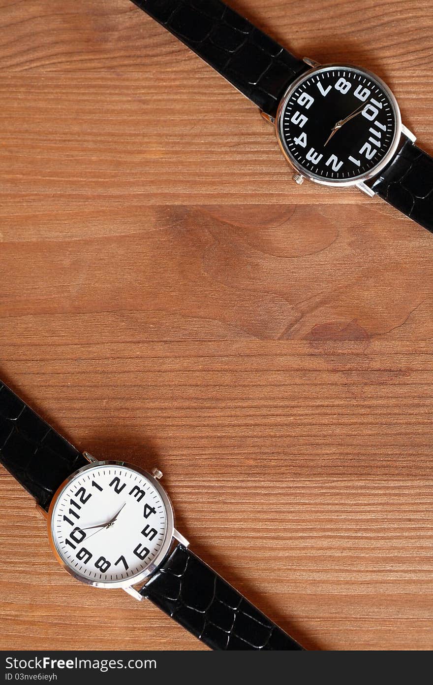 Pair of modern black and white wristwatches on wooden surface