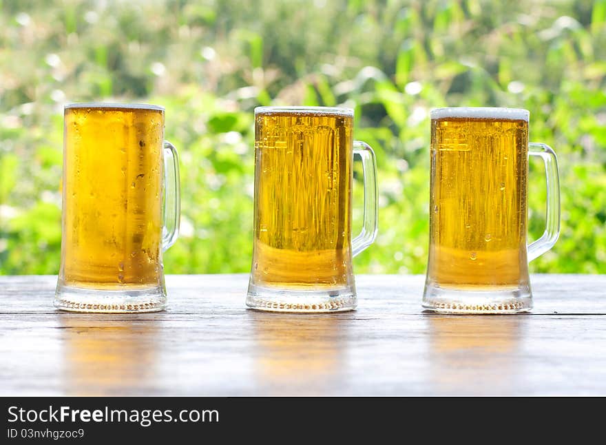 Three mug of beer at the table close-up, background is out of focus