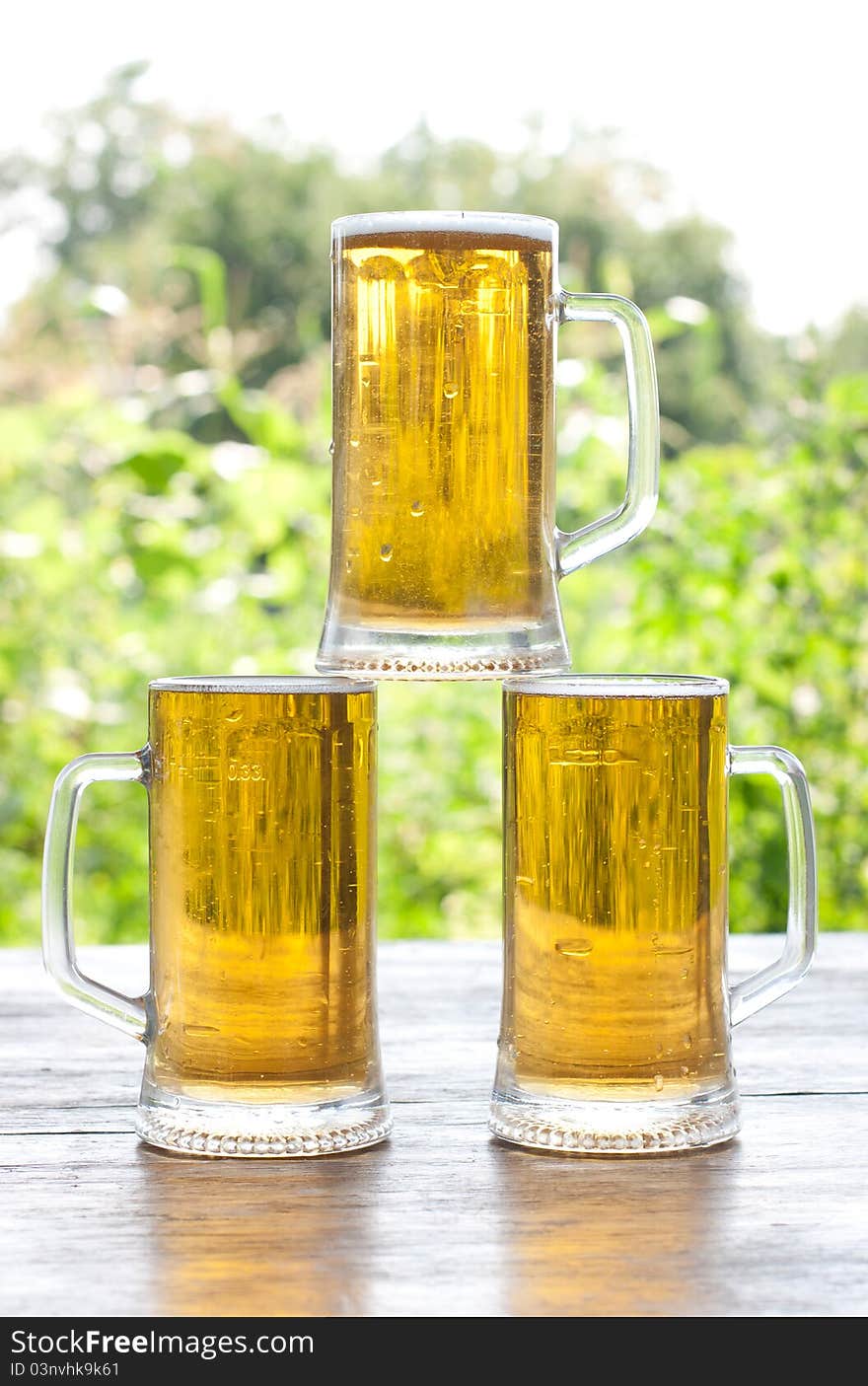 Three mug of beer at the table close-up, background is out of focus