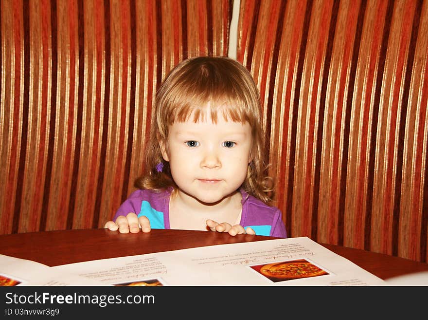 Little girl sitting in a cafe and looking at menu. Little girl sitting in a cafe and looking at menu