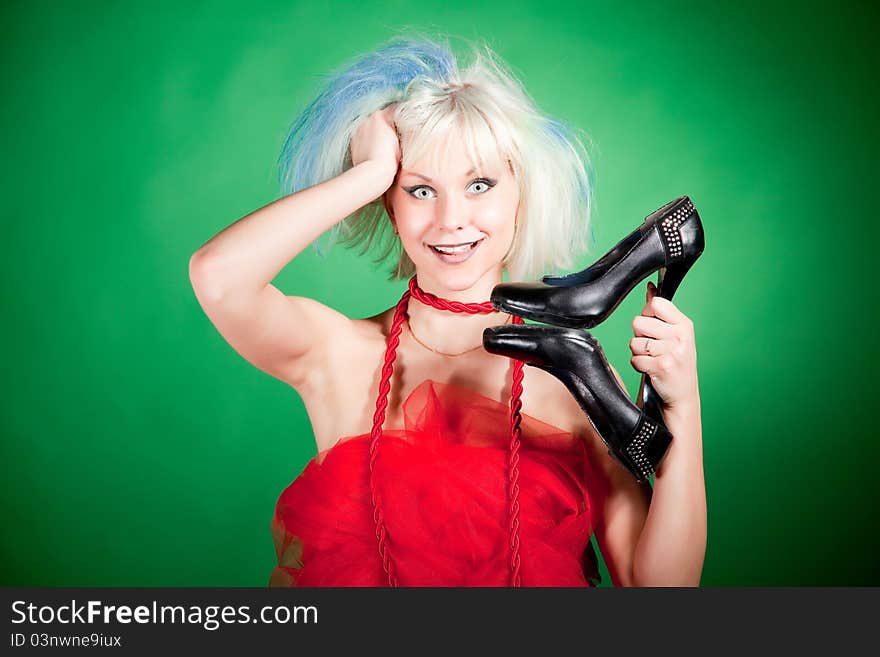 Blonde crazy girl holding shoes, portrait shot over green background