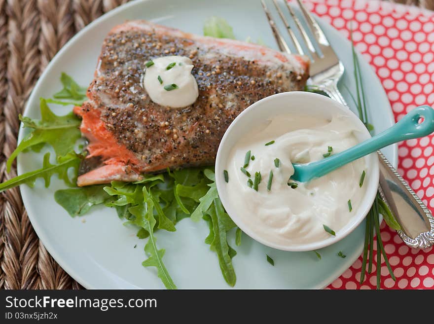 A broiled piece of salmon sits on a bed of lettuce next to a homemade dip of mayonnaise and yogurt with fresh chives, a fork rests on the side after a bite has been taken. A broiled piece of salmon sits on a bed of lettuce next to a homemade dip of mayonnaise and yogurt with fresh chives, a fork rests on the side after a bite has been taken.