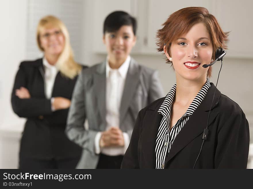 Pretty Red Haired Businesswoman with Headset and Colleagues Behind in Office Setting. Pretty Red Haired Businesswoman with Headset and Colleagues Behind in Office Setting.