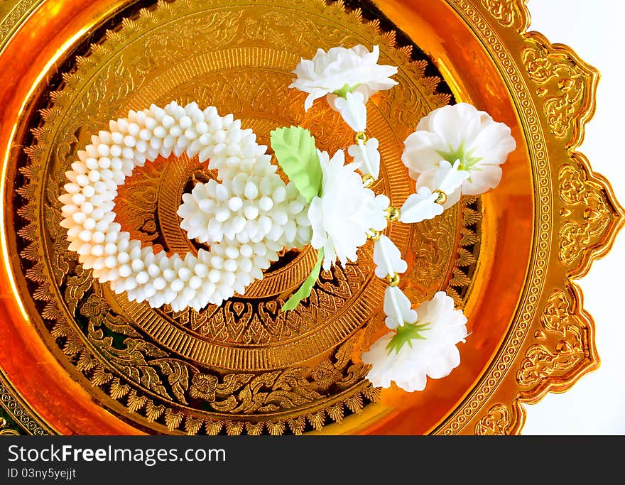 Jasmine garland on gold tray with pedestal, white background.