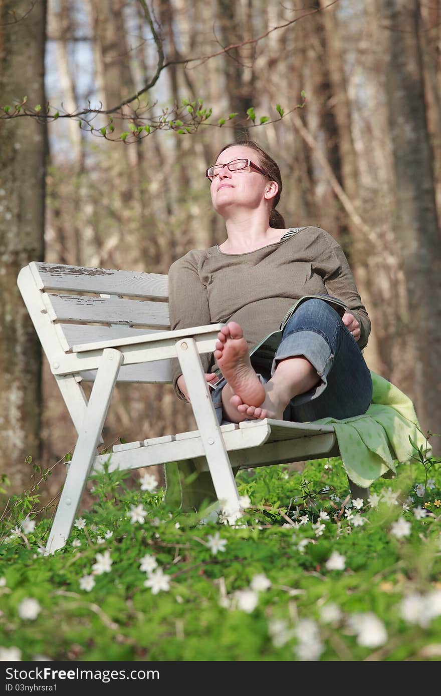 Woman sitting on a sofa in the wood in springtime. She is reading a magazine in the sunlight. Woman sitting on a sofa in the wood in springtime. She is reading a magazine in the sunlight