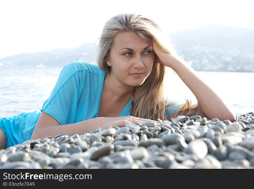 Beautiful young woman posing on stones near sea