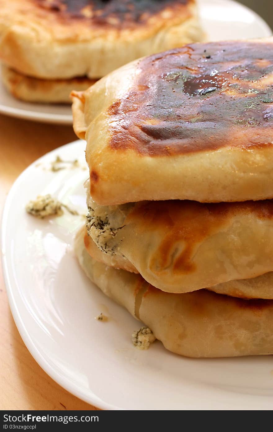 On the plate is a stack of pies. One of the pie filling is broken and fallen. In a stack of three pies. In the background are two more pie on the plate.