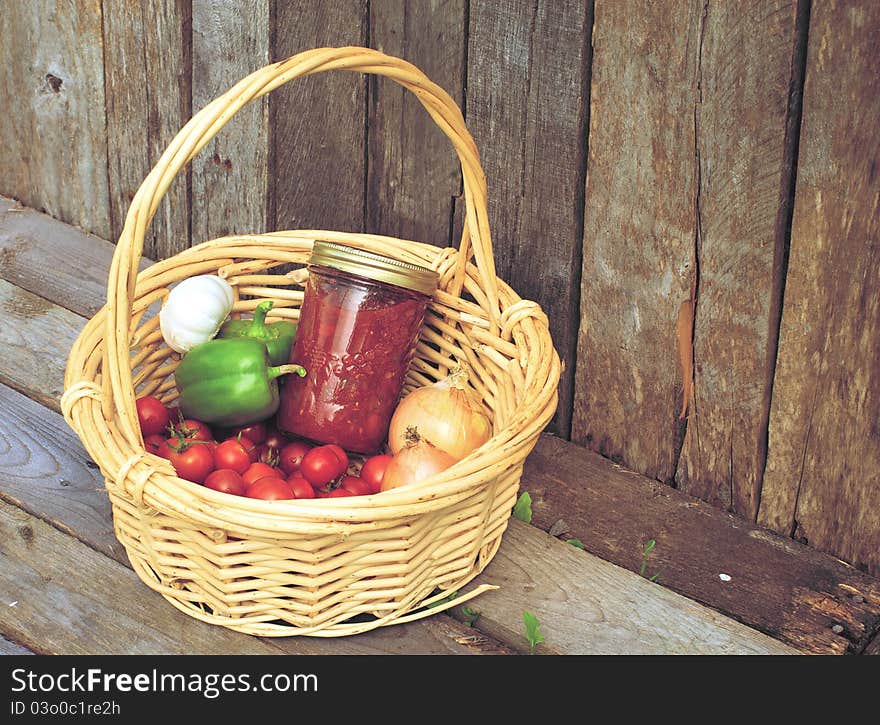 Image of a basket of freshly picked organic vegetables and a jar of homemade salsa on a rustic background. Image of a basket of freshly picked organic vegetables and a jar of homemade salsa on a rustic background.