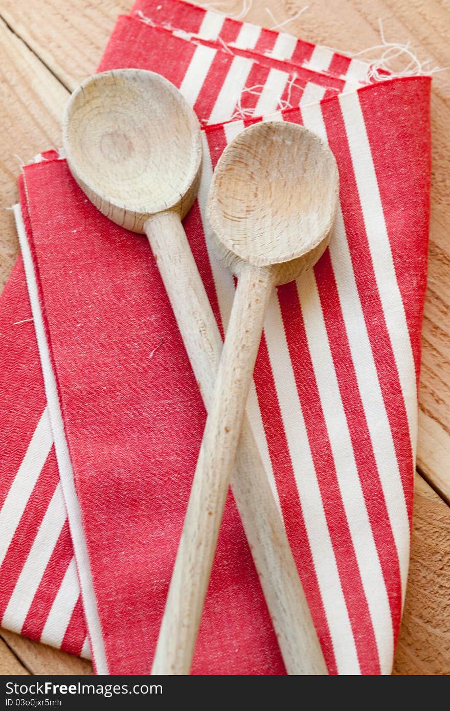 Two wooden spoons rest on a red striped kitchen towel. Two wooden spoons rest on a red striped kitchen towel.