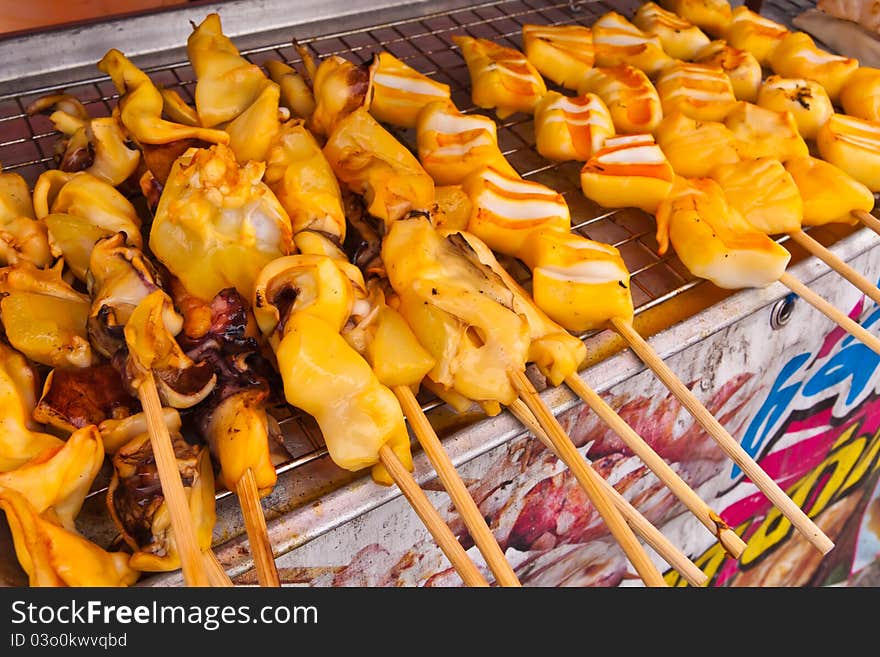 Yellow grilled squids in group with wooden stick on grill. Yellow grilled squids in group with wooden stick on grill