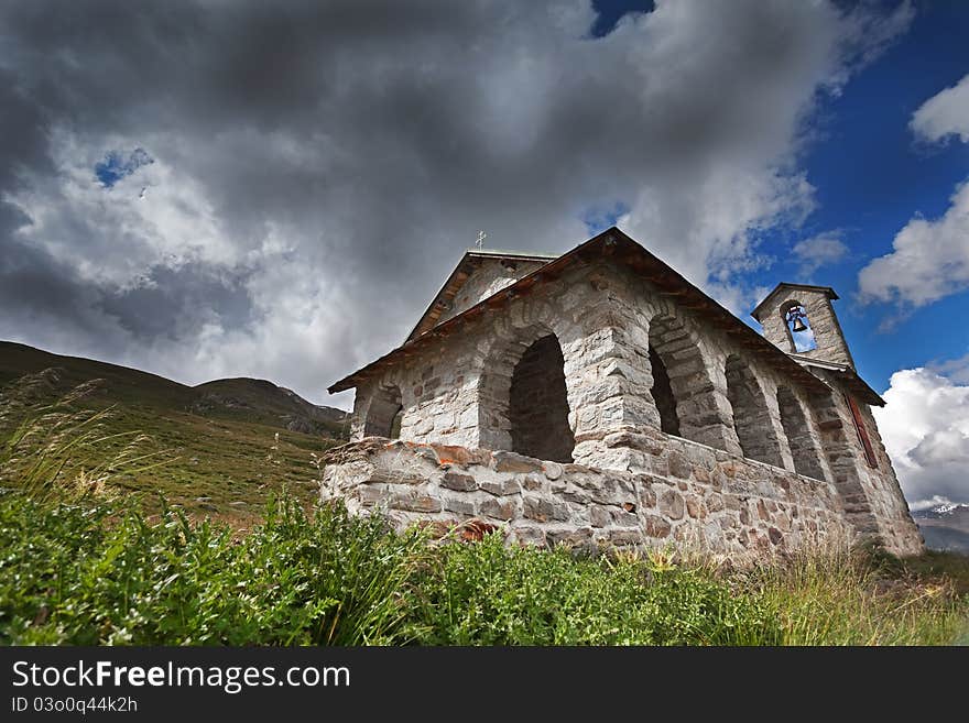 A small church in high mountain during summer with a cloudy sky