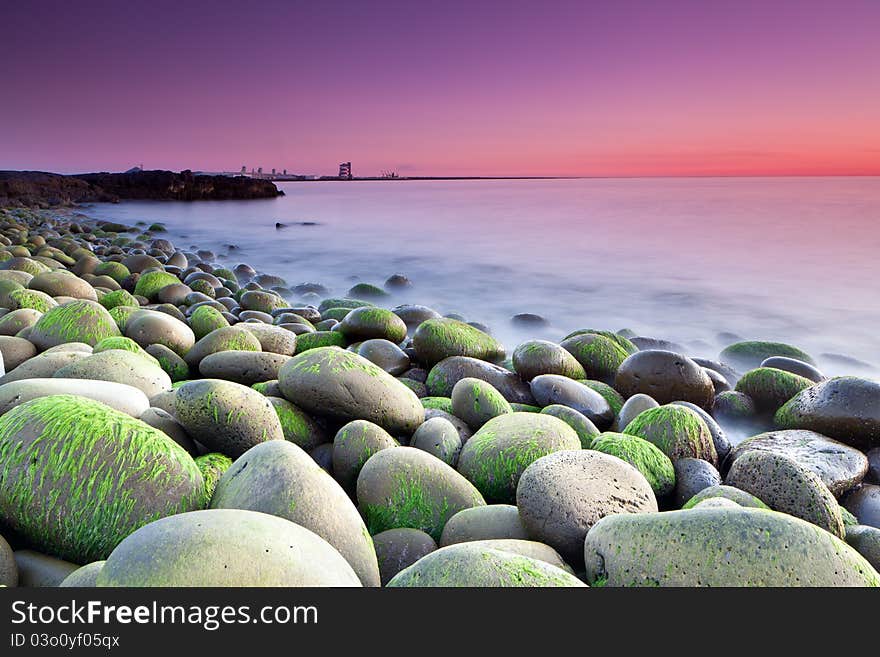 Sunset picture in Hvaleyri , Seascape picture taken just after sunset of the rocks and slime. A factory in the background. Taken with Tilt-shift lens to maximize focus on both foreground and the buildings far away. Sunset picture in Hvaleyri , Seascape picture taken just after sunset of the rocks and slime. A factory in the background. Taken with Tilt-shift lens to maximize focus on both foreground and the buildings far away.