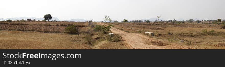 A panoramic view with a mud road with grass lands on either side and a chain of mountains in the distance. A panoramic view with a mud road with grass lands on either side and a chain of mountains in the distance.