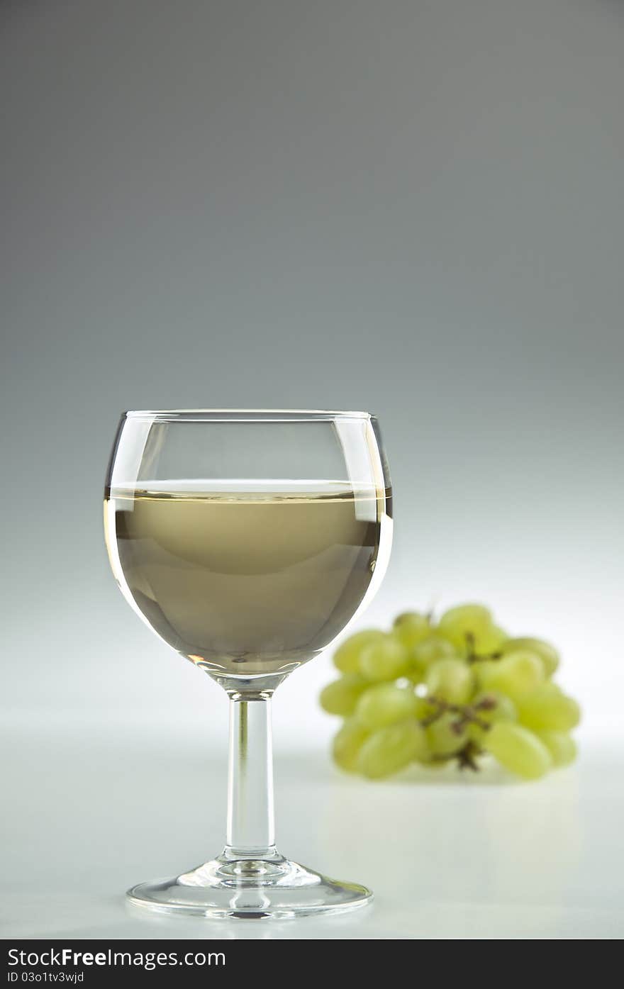 Glass of white wine and grapes in the background. Glass of white wine and grapes in the background