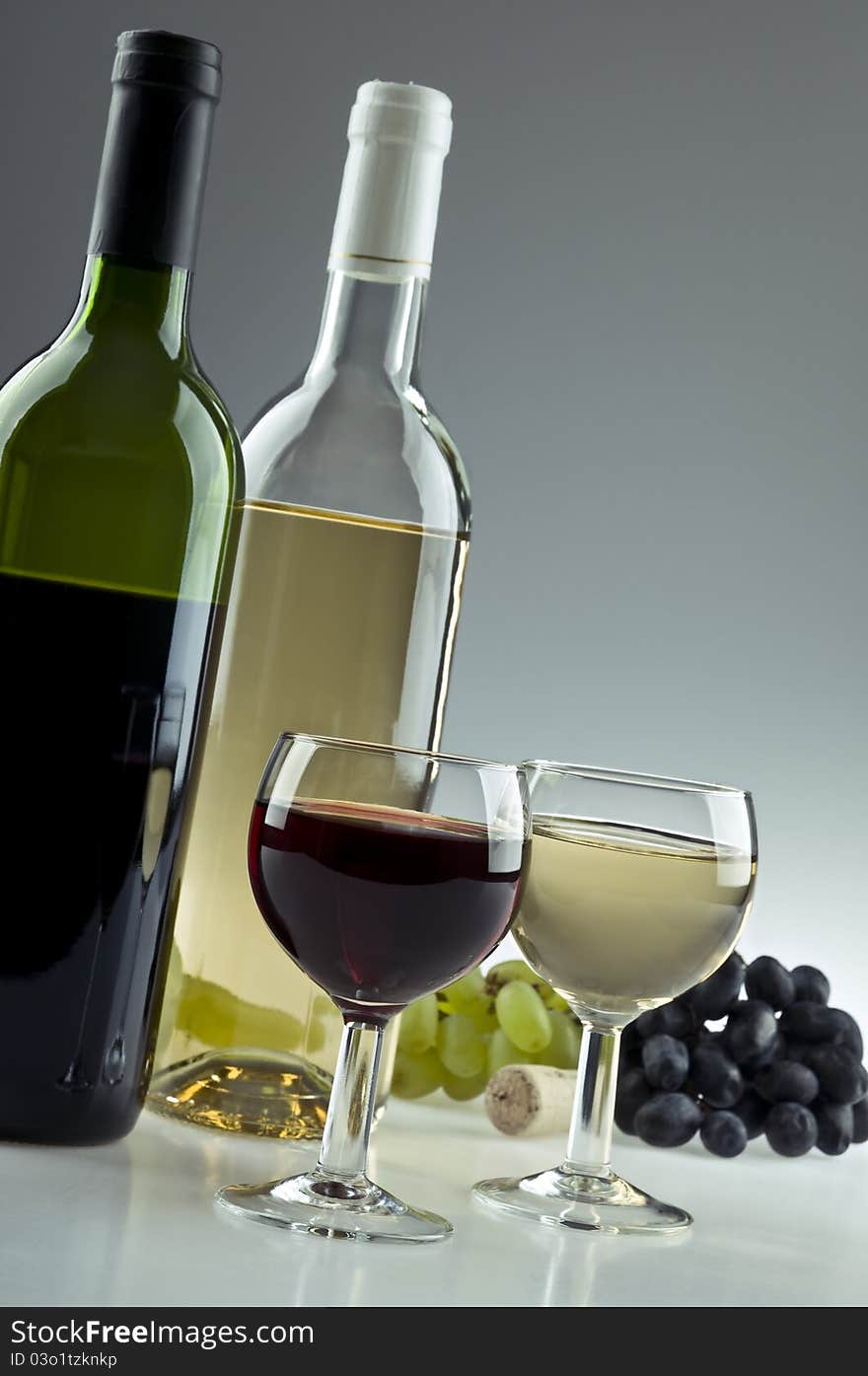 Red and white wine bottles and glasses with grapes