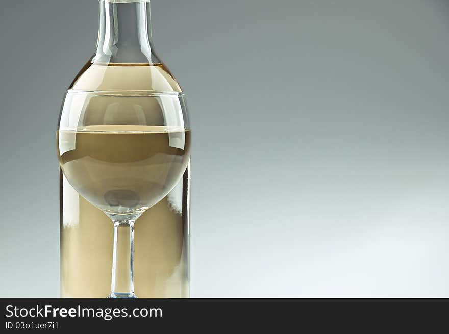 A bottle and a glass of white wine, glass in front of the bottle