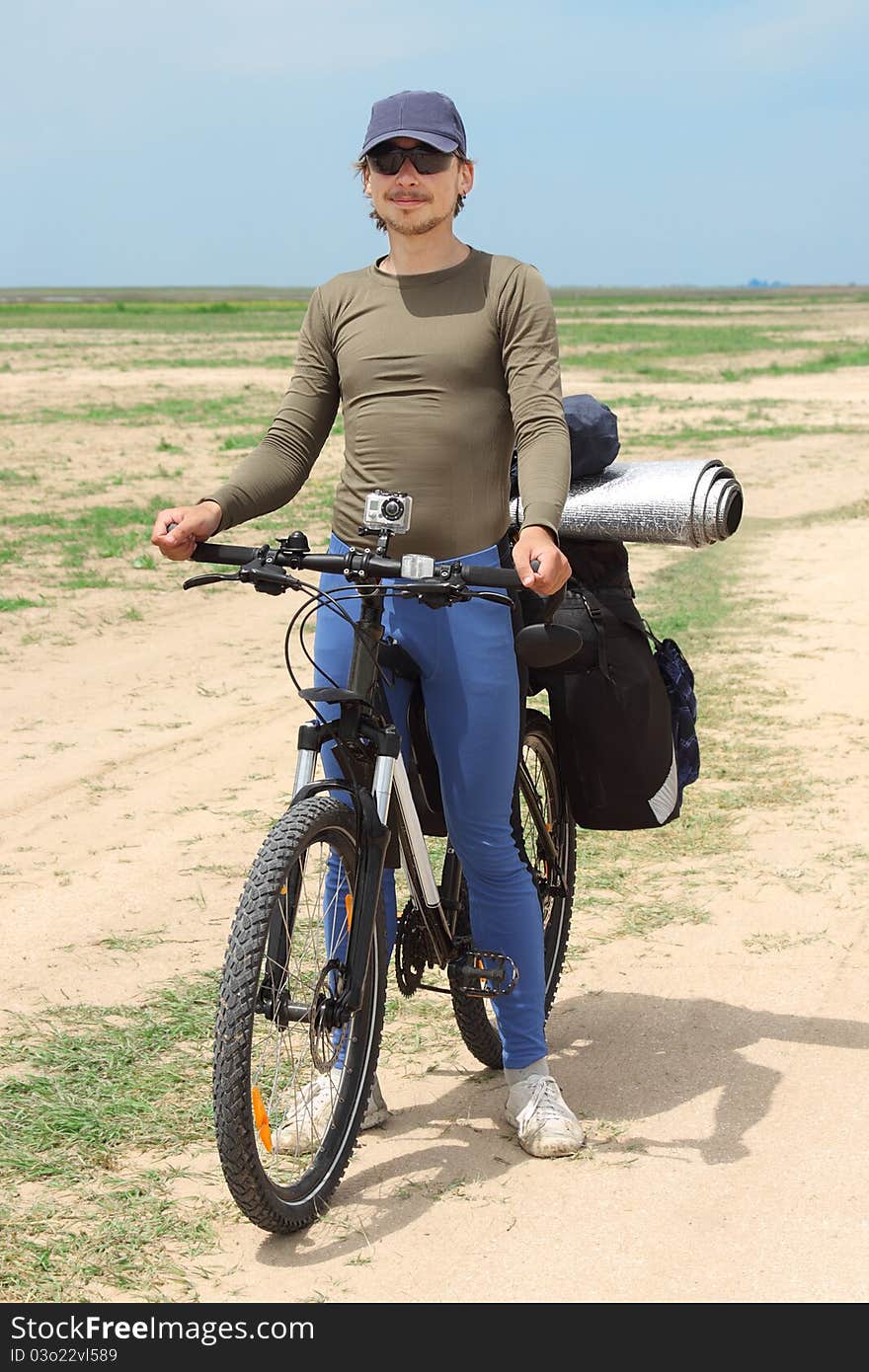 Bicycle tourist standing on road, blue sky and horizon