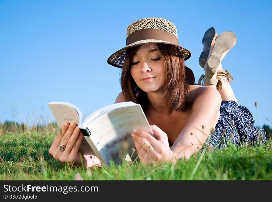 Young nice attentive woman lies on green grass and reads book