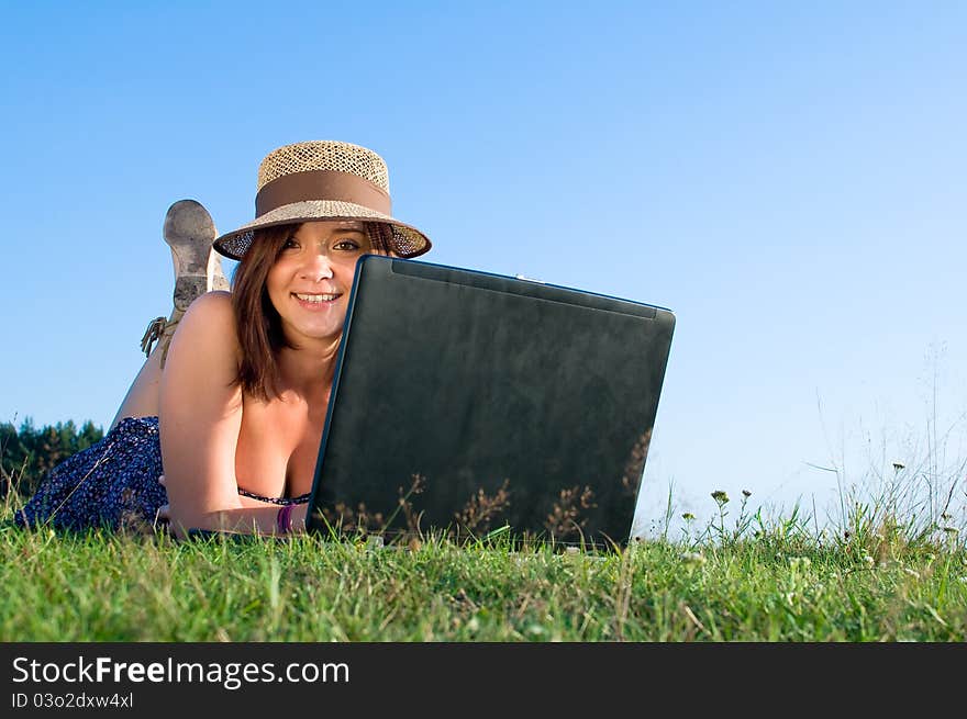 Smiling beautiful woman laying on grass and working on laptop