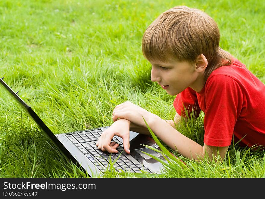 Young boy with laptop lying on grass