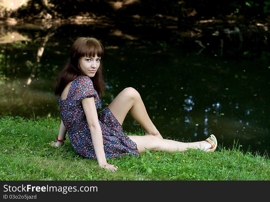 Beautiful girl sitting on bank of a river in summer