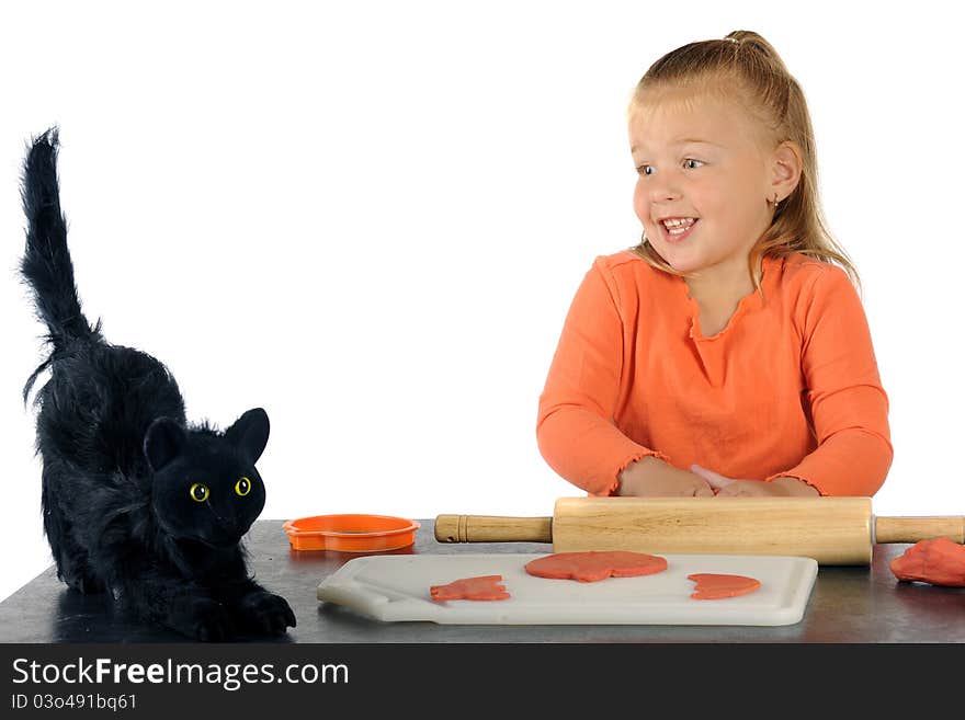 An adorable preschooler skittish with a furry black cat while making Halloween cookies from orange modeling clay. An adorable preschooler skittish with a furry black cat while making Halloween cookies from orange modeling clay.