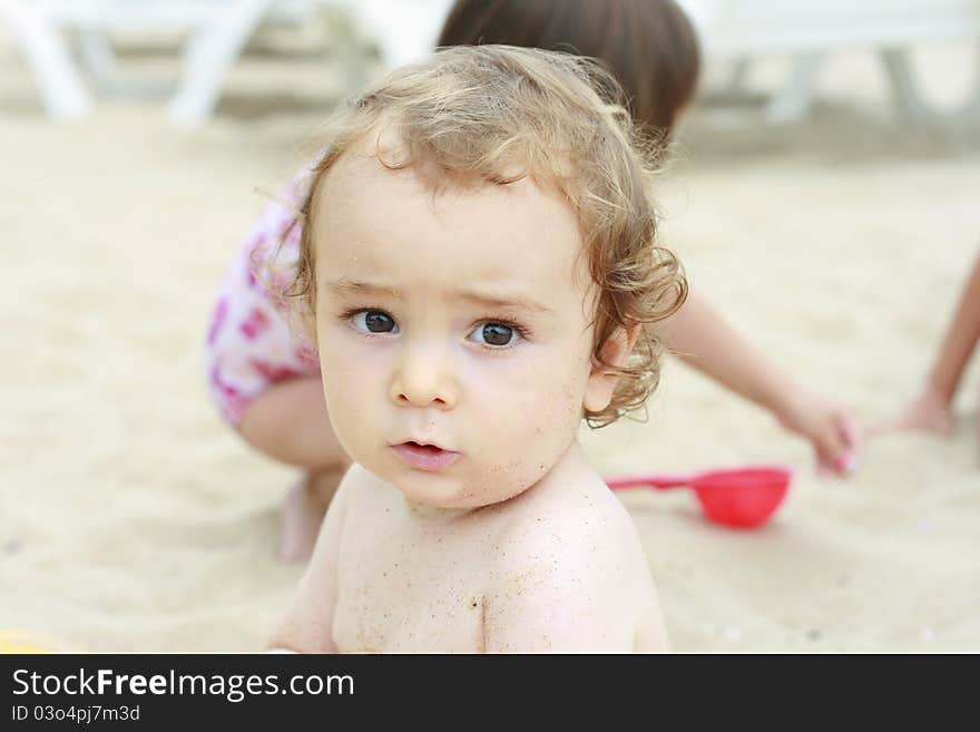 Baby boy looking at the camera with sand on his face. Baby boy looking at the camera with sand on his face