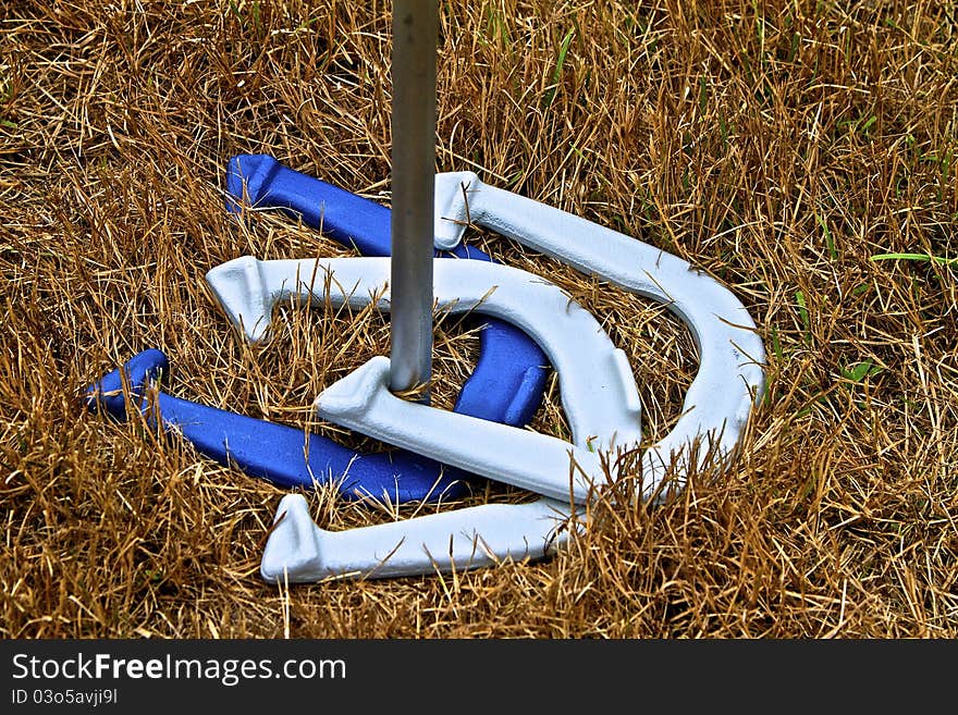 Three horseshoes around stake, one dark blue and two light blue, atop golden grasses. Three horseshoes around stake, one dark blue and two light blue, atop golden grasses