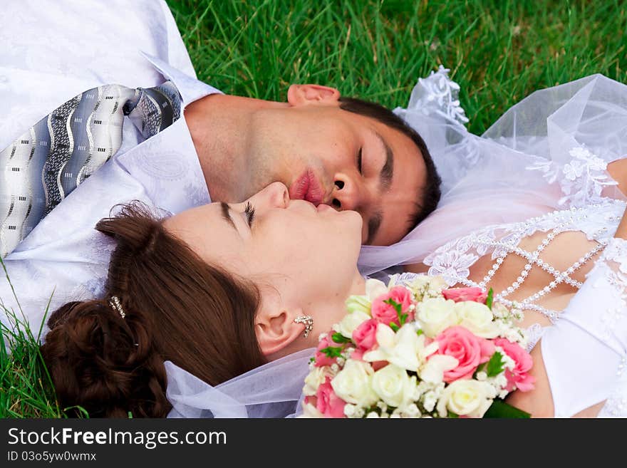 Happy bride and groom lying on a green grass