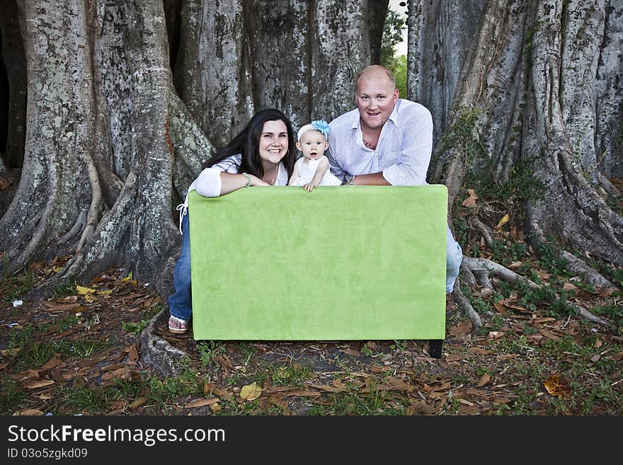 A portrait of a happy young family leaning over back of a love seat under a tree. A portrait of a happy young family leaning over back of a love seat under a tree.