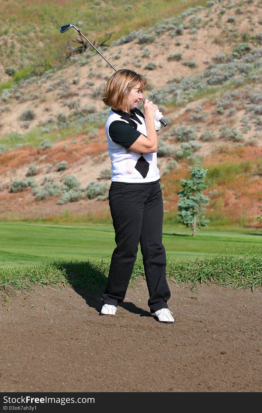 Blond female golfer playing a shot out of the bunker